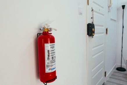 A red powder fire extinguisher mounted on a white wall beside a white door